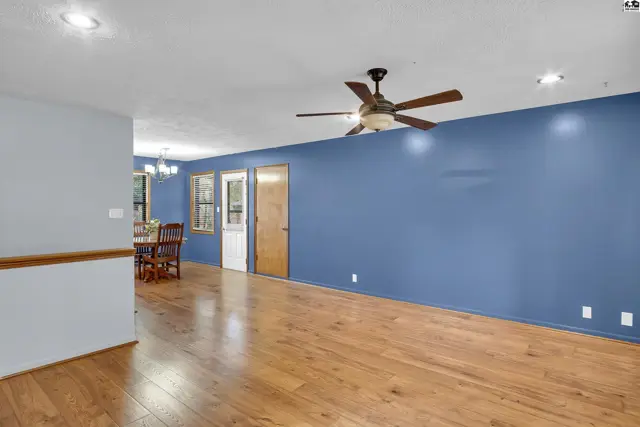 Spacious living area with hardwood floors, a ceiling fan, and blue accent wall.