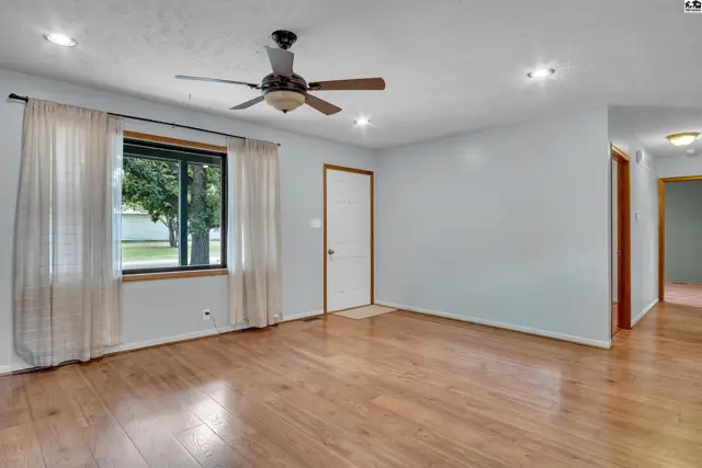 Spacious living area with hardwood floors, a ceiling fan, and a large window.