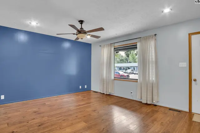 Spacious room with hardwood floors, a ceiling fan, and a large window.