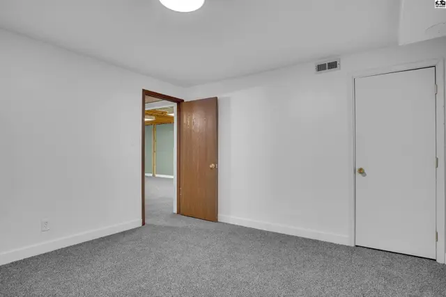 Carpeted room with white walls, a wooden door, and a white door.