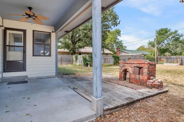 Covered patio with ceiling fan overlooks a brick outdoor fireplace and backyard.