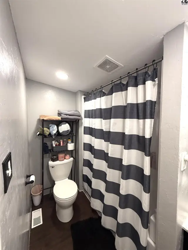 This bathroom features a toilet, shower with a striped curtain, and a metal shelving unit.