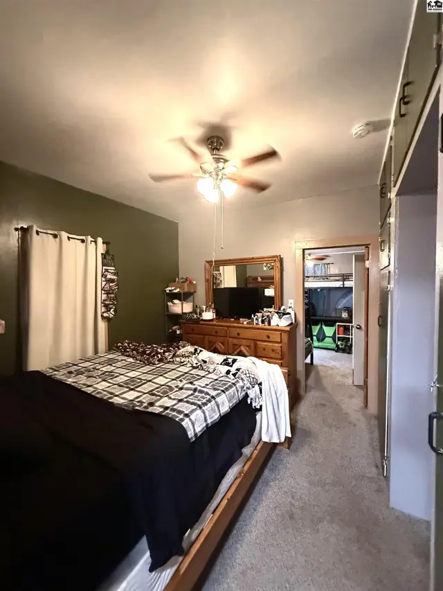 This bedroom features a ceiling fan, dresser, and access to another room.