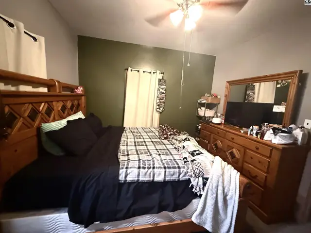This bedroom features a wooden bed frame, dresser, and mirror with a ceiling fan.