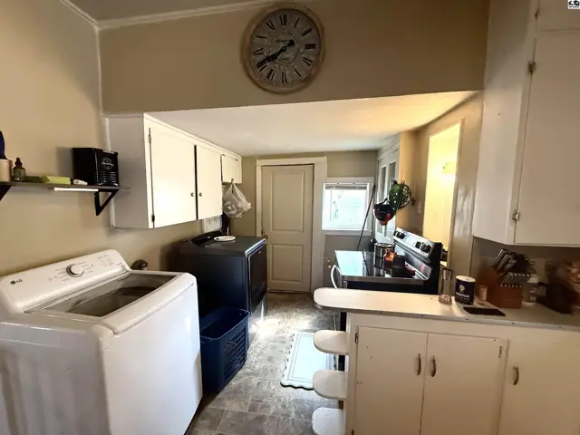 This kitchen features white cabinetry, a black stove, and a white washing machine.
