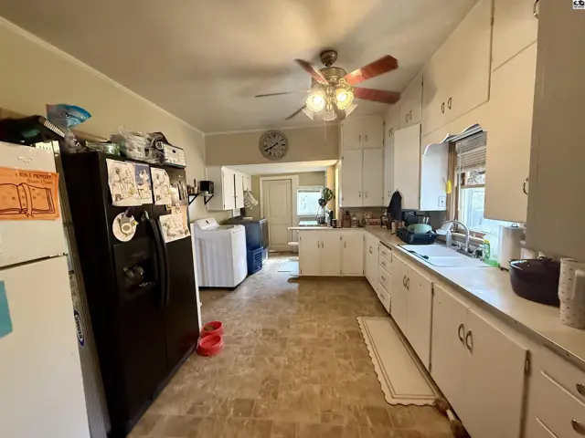 This kitchen features white cabinetry, a double sink, and a ceiling fan.