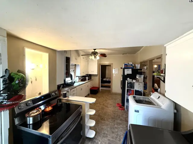 Spacious kitchen features white cabinetry, a stove, refrigerator, and a washing machine.