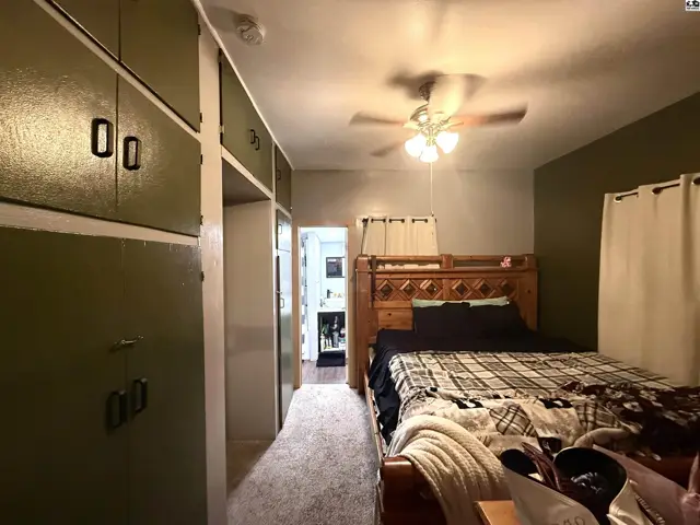 Bedroom with built-in green cabinets, a ceiling fan, and a wooden bed frame.