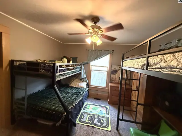 This bedroom features two bunk beds, a dresser, and a ceiling fan.
