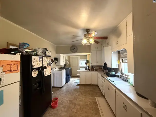 This kitchen features white cabinetry, a ceiling fan, and a laundry area.