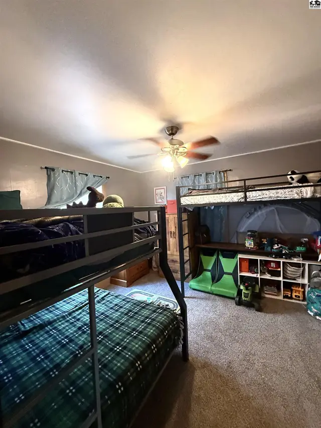 Two bunk beds with plaid bedding fill this room with carpeted floors and a ceiling fan.