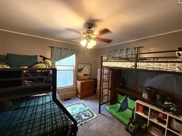 Two bunk beds with metal frames and green bedding fill this room with carpet.