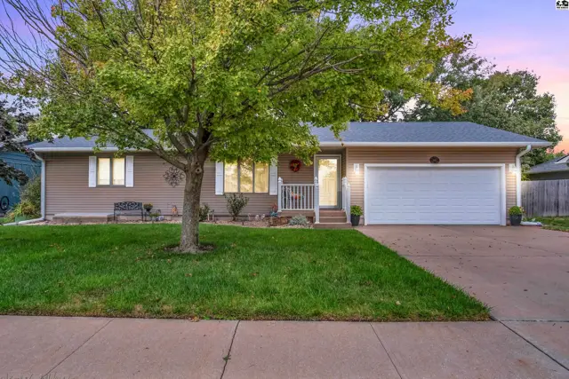 This tan-sided ranch home features a two-car garage and mature landscaping.