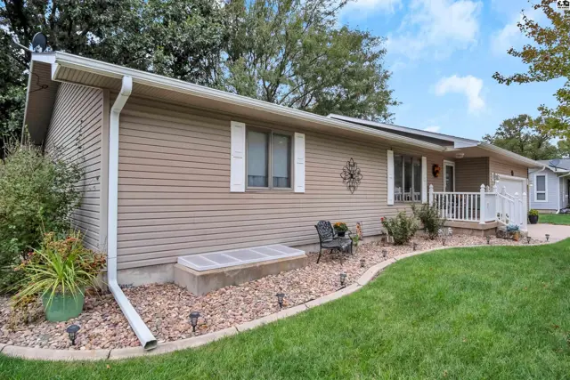 This single-story home features tan vinyl siding, a white-trimmed entryway, and a landscaped front yard.