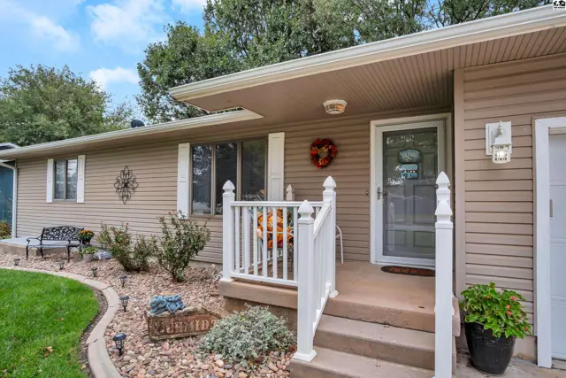 This tan vinyl-sided home features a covered porch with white railings and a front door with a screen.