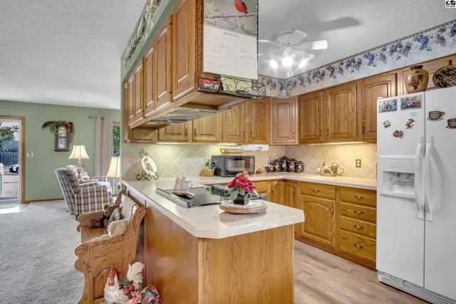 This kitchen features light wood cabinetry, a central island with a cooktop, and a white refrigerator.