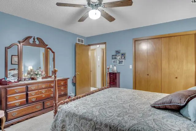 Spacious bedroom features a ceiling fan, large closet, and a dresser with a tri-fold mirror.