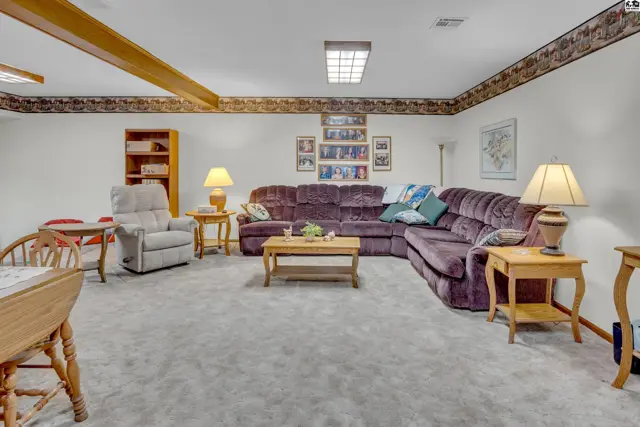 Spacious living area with plush carpeting, a sectional sofa, and decorative wood beams.