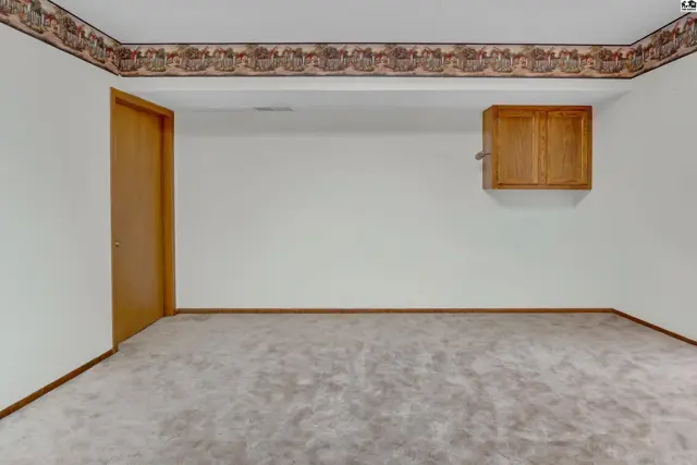 Carpeted room with white walls, wood-paneled door, and a small wooden cabinet.