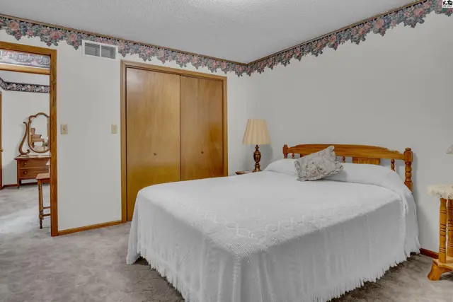 This bedroom features a wooden bed frame, a double closet, and floral wallpaper border.