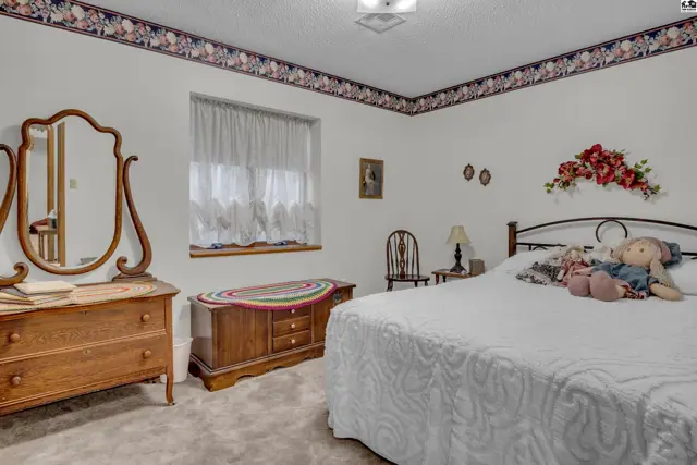 This bedroom features a dresser, mirror, chest, and a bed with a white comforter.
