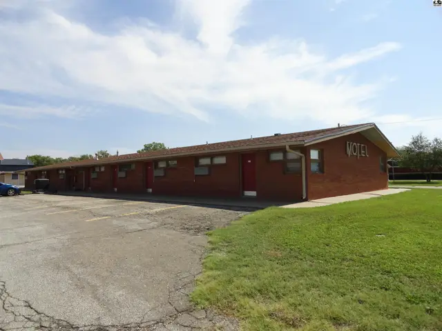Brick building with multiple doors and windows, a pitched roof, and a paved parking lot.