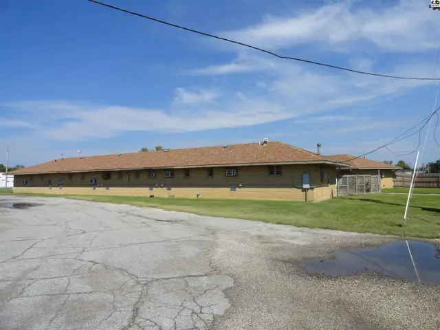 This tan building features a brown shingled roof and multiple air conditioning units.