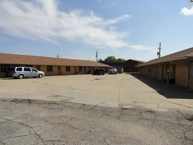 Two single-story buildings with asphalt shingle roofs flank a paved parking lot.