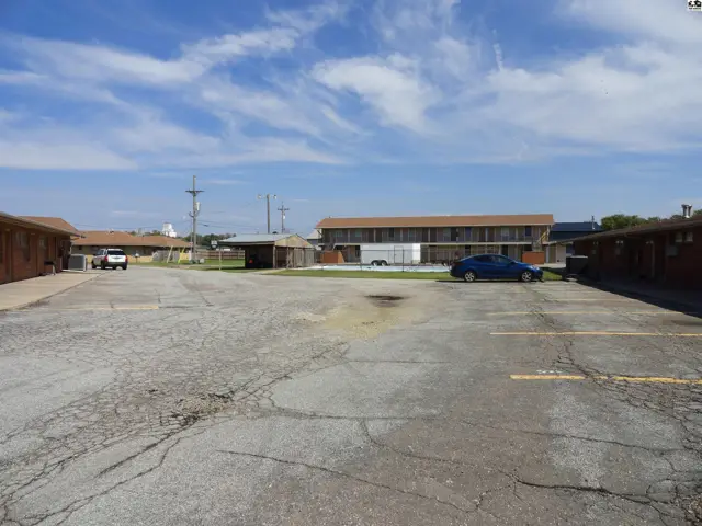 Asphalt parking lot with painted lines fronts brick buildings and a small pool.