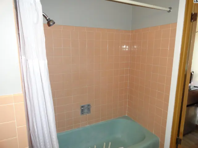 Bathtub with a shower curtain and pale pink tiled walls.