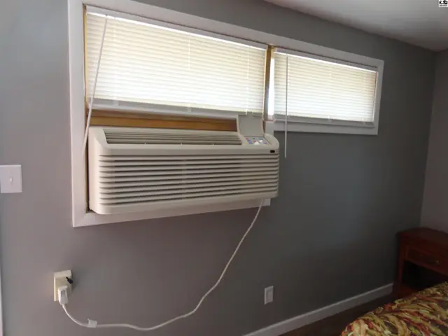 Window air conditioning unit installed below two blinds-covered windows.