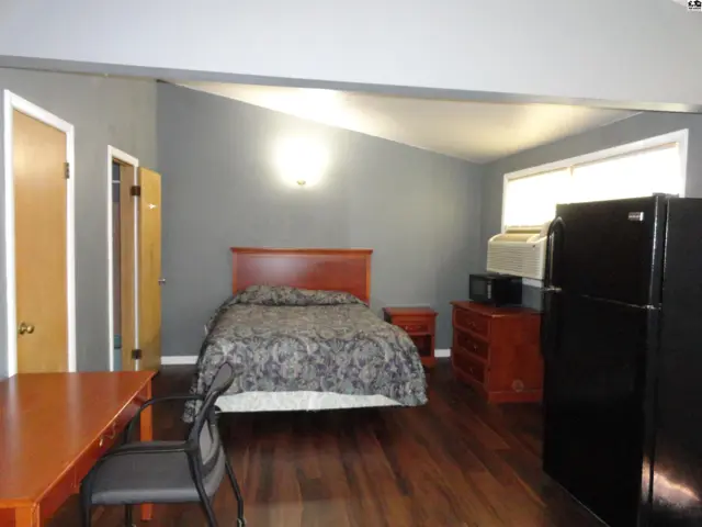 This room features a bed, dresser, refrigerator, microwave, and desk.