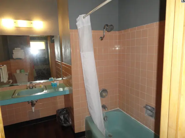 This bathroom features a light blue tub, pink tiled walls, and a vanity with a light blue sink.