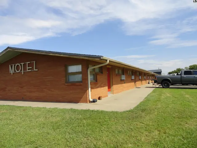 Brick motel building with a paved walkway and grassy lawn.
