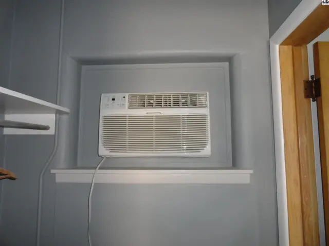 Window air conditioning unit installed in a recessed wall niche with a wooden door frame.