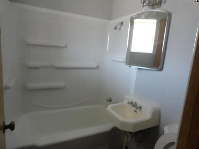 White bathtub with shower, sink, and mirror in a light-colored bathroom.
