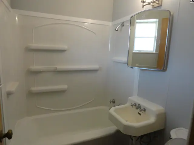 White bathtub with shower surround and a pedestal sink with mirror.