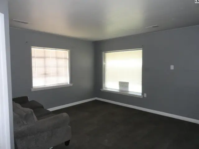 This room features gray walls, carpeted flooring, and two large windows.