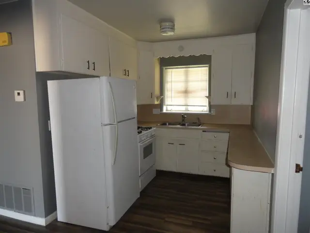 White appliances and cabinets complement the laminate countertops and dark wood flooring in this kitchen.