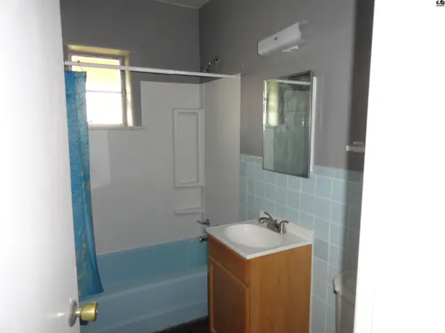 This bathroom features a light blue tub, white shower surround, and a wooden vanity.