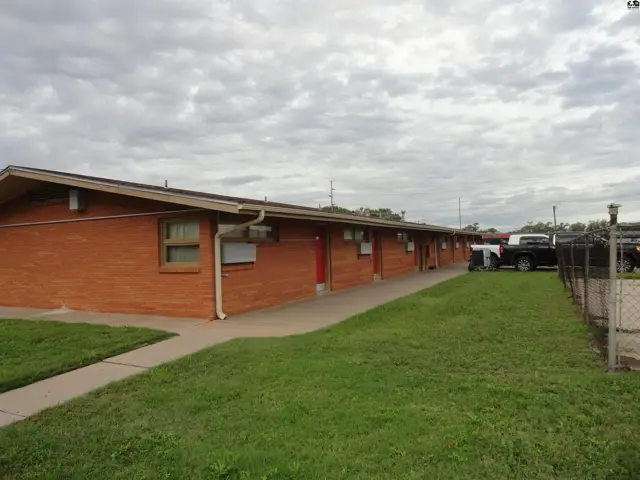 Brick building with multiple doors and windows, a paved walkway, and a grassy lawn.