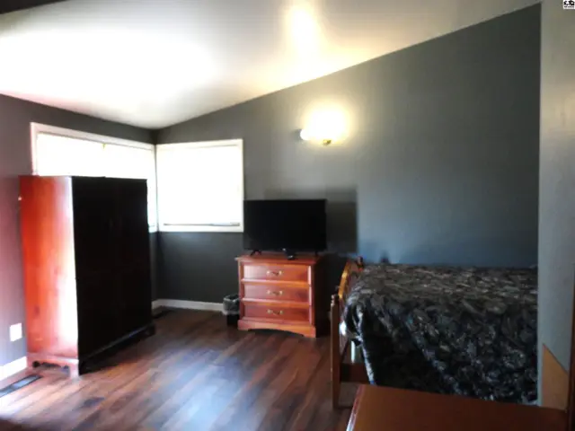 Spacious room with dark grey walls, wood flooring, and a large window.