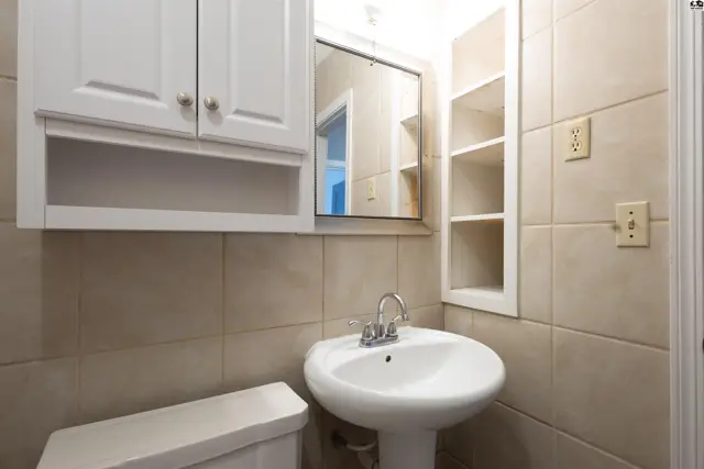 White pedestal sink and toilet are set against tiled walls with a white medicine cabinet.