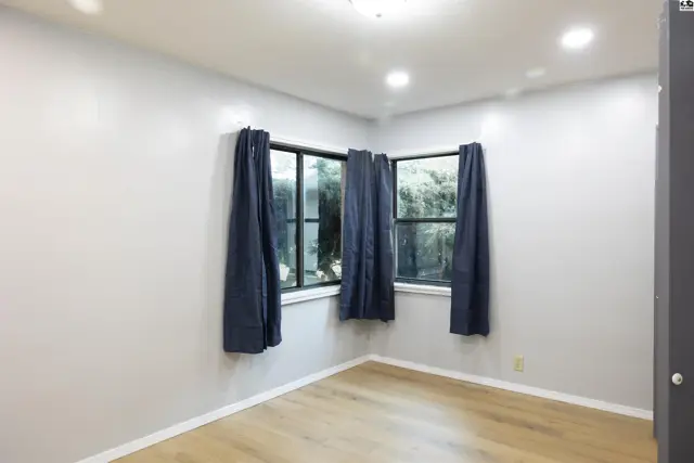 This room features light wood-look flooring, white walls, and two windows with dark blue curtains.