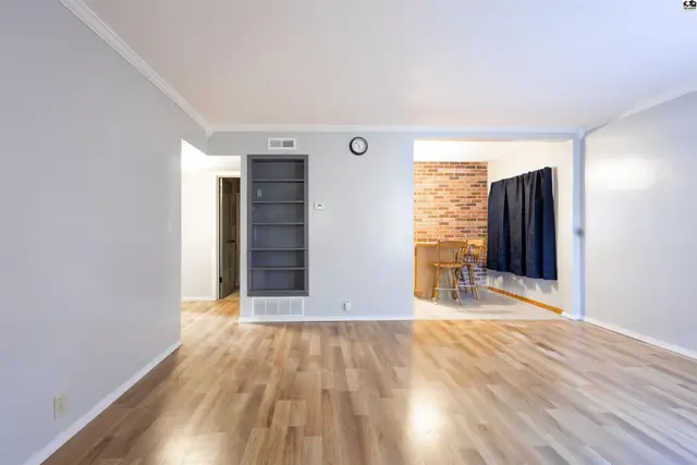 Light-filled living area with wood floors and built-in shelving opens to a dining space.