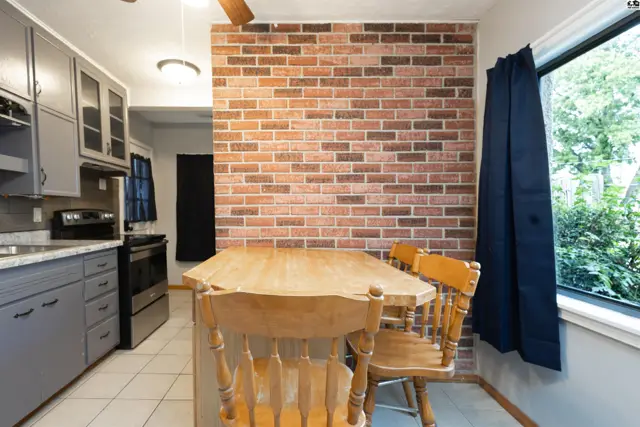 A wooden table and chairs sit before a red brick accent wall in this kitchen area.