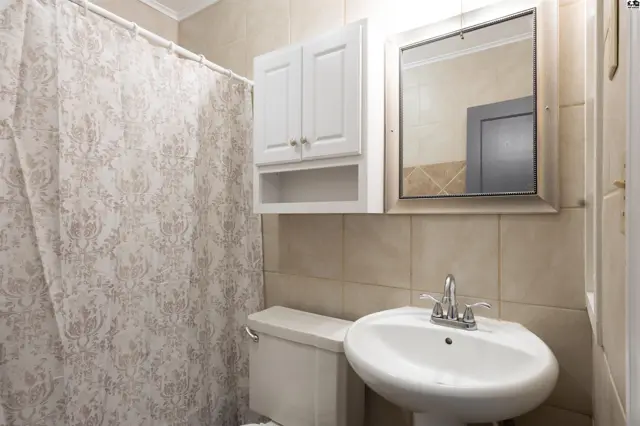 This bathroom features a pedestal sink, white vanity, and tiled walls.
