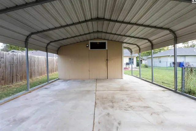 Metal carport with concrete floor attached to a tan sided structure.