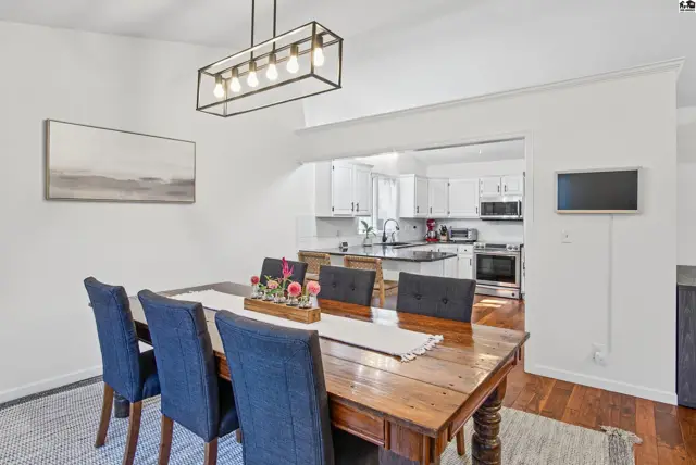 A dining area with a chandelier overlooks a white kitchen with stainless steel appliances.
