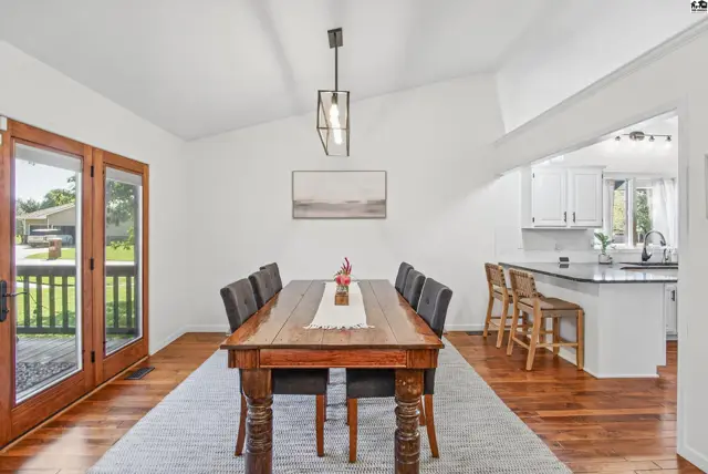 Spacious dining area with a vaulted ceiling, wood floors, and a view into the kitchen.